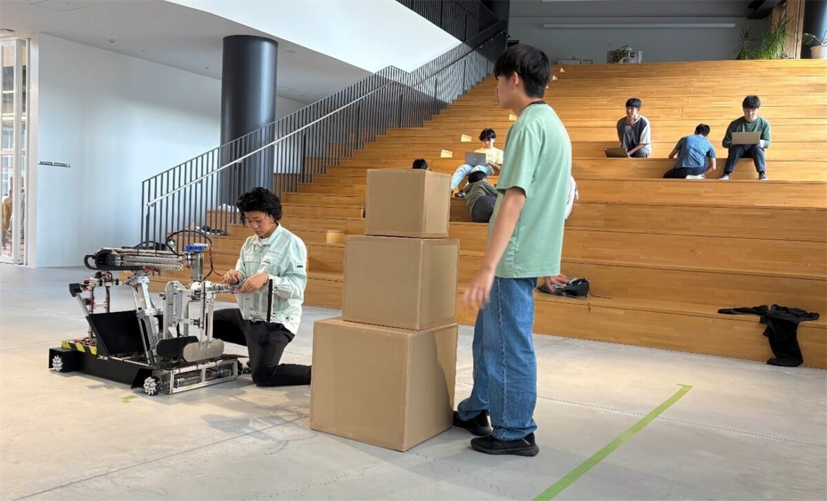 キャンパスでロボットの調整をする2年生と見守る1年生（Bチーム）